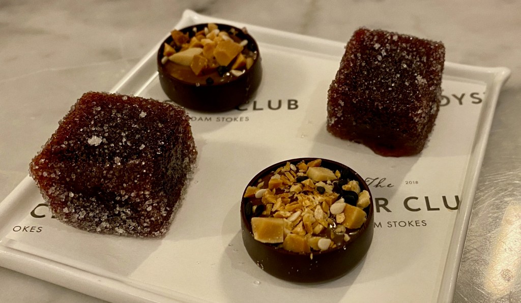 4 petit fours, 2 purple cubes of plum jelly, and two round chocolates topped with chopped nuts