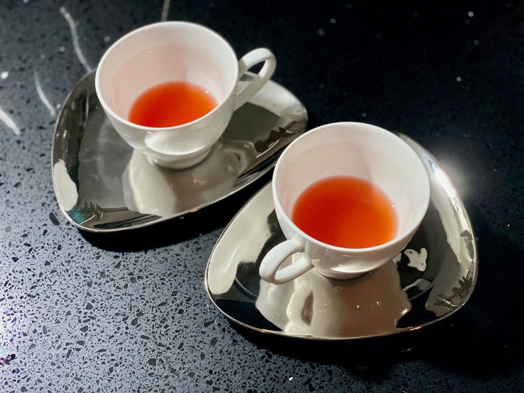 White tea cups filled with strawberry coloured clear liquid on silver teardrop saucers
