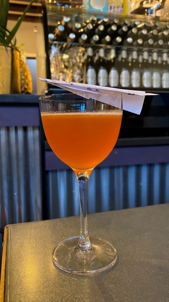 Pink cocktail with a paper aeroplane perched on the glass